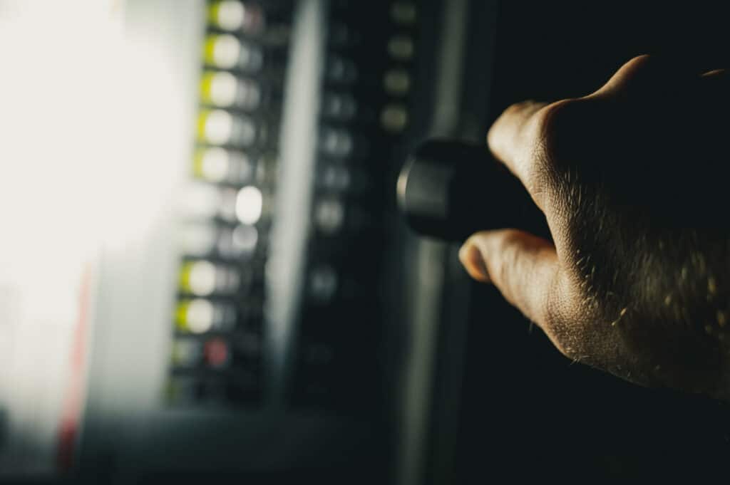 Power interruptions surge with silhouette of hand holding a flashlight aimed at a fuse box.
